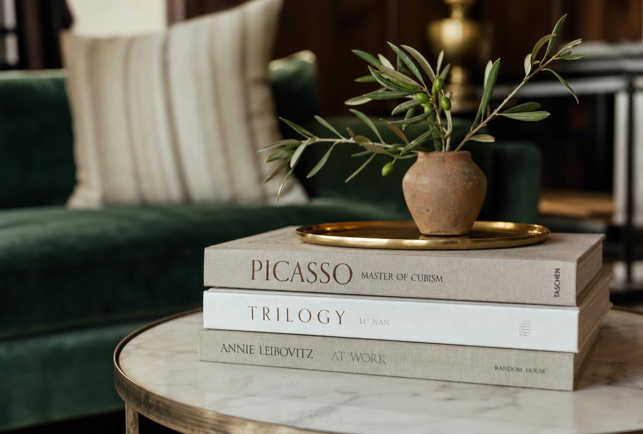 Coffee Table Books — Stack of three hardcover books in muted tones on a wooden coffee table with a ceramic bowl and candle